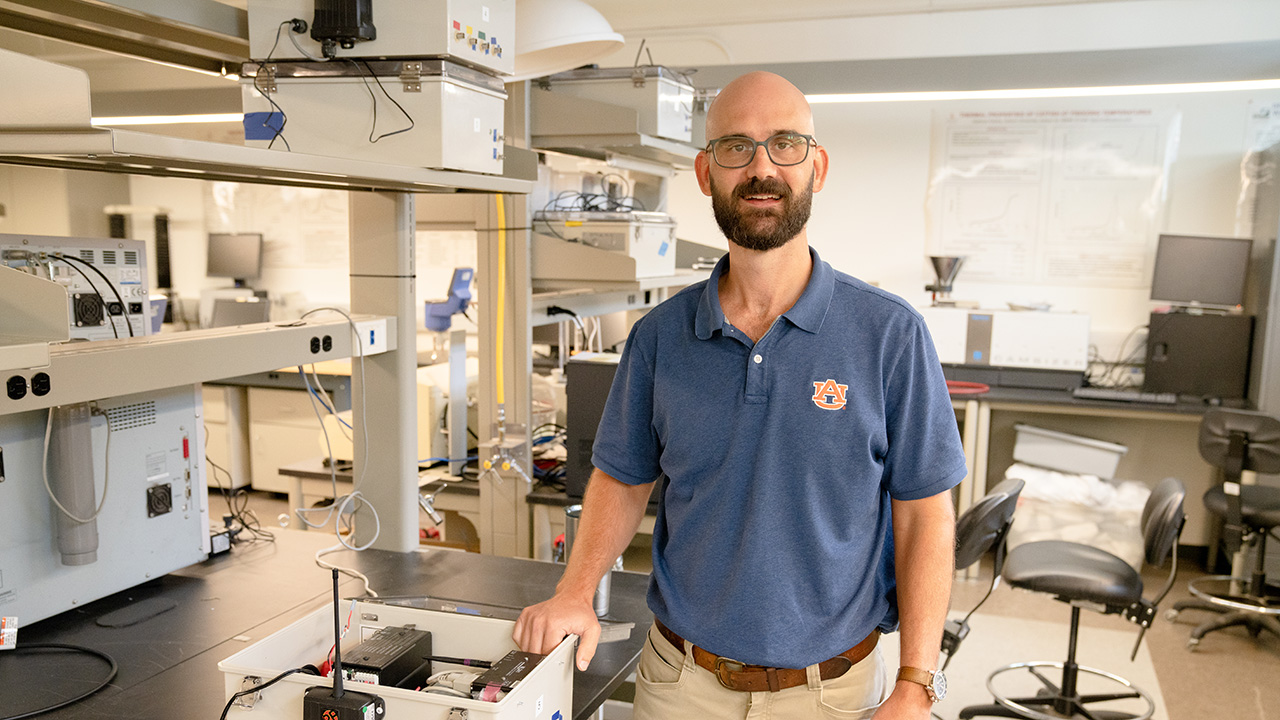 Bald man with beard and glasses stands in research lab