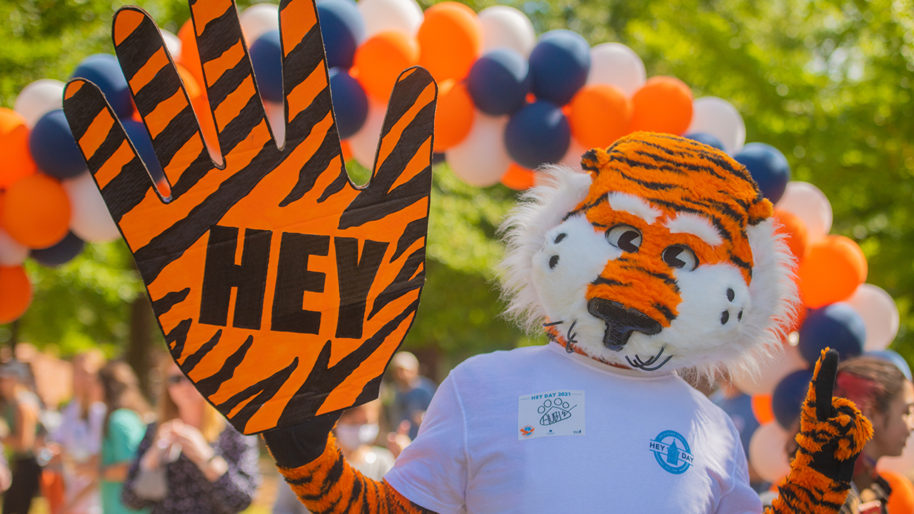 Aubie holding a foam finger that says Hey Day on it. 