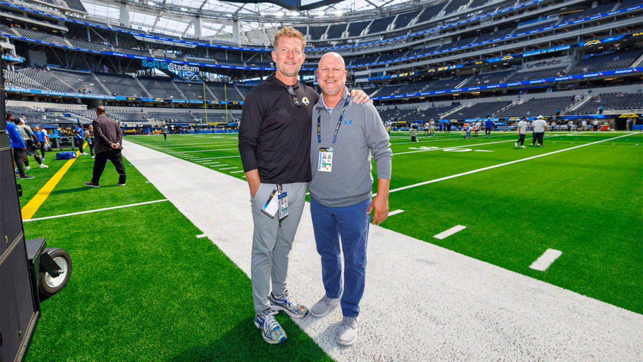 Los Angeles Rams GM Les Snead ’94 (left) and Los Angeles Chargers GM Joe Hortiz ’98 stand on a field at a preseason game.