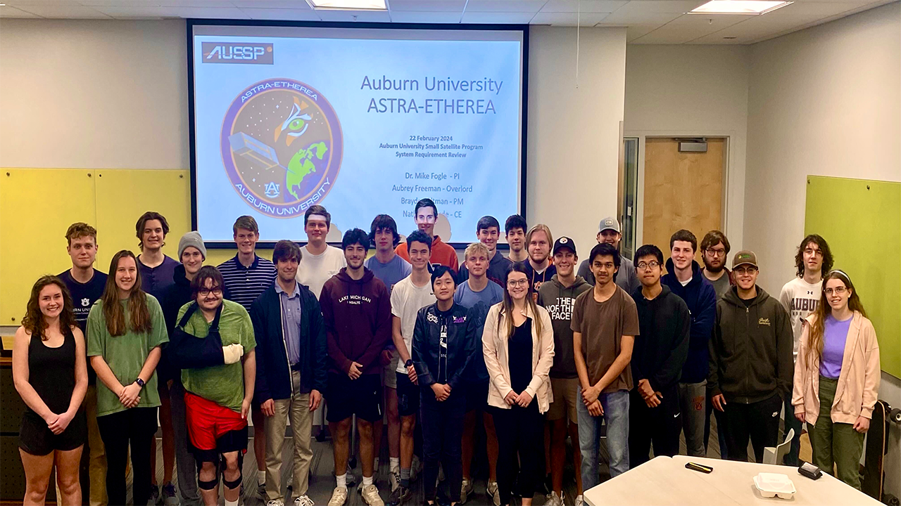 A group of undergraduate students take a photo in a physics classroom. 