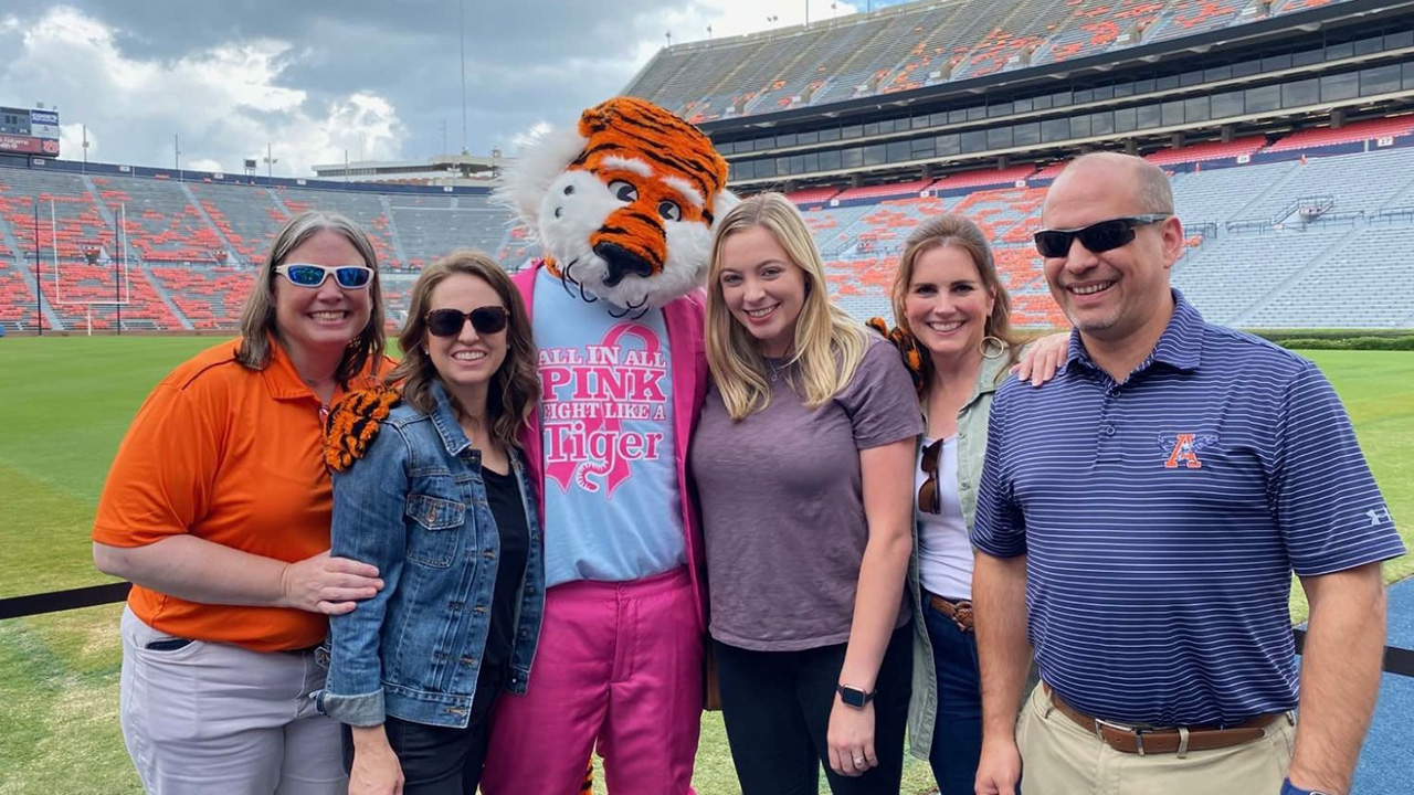 Four women and one man stand posing with Aubie on the football field