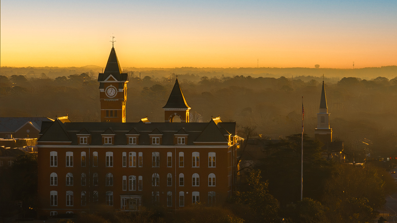 An aerial shot of Samford Hall with a hazy sunset behind it
