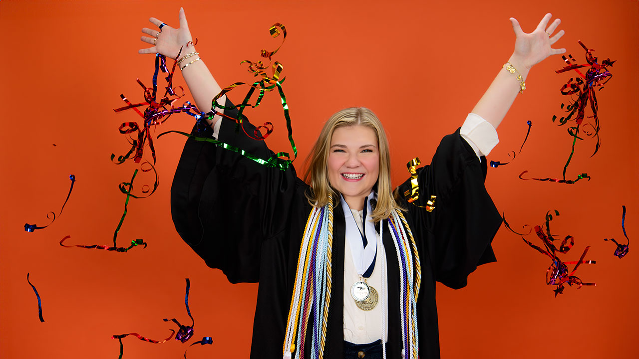 A girl in graduation regalia celebrates with confetti.