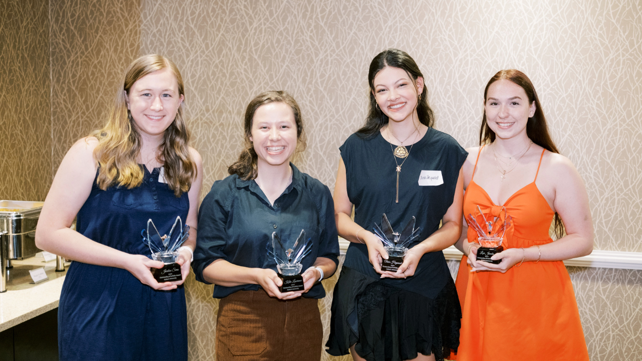 Four students stand beside one another holding trophies.