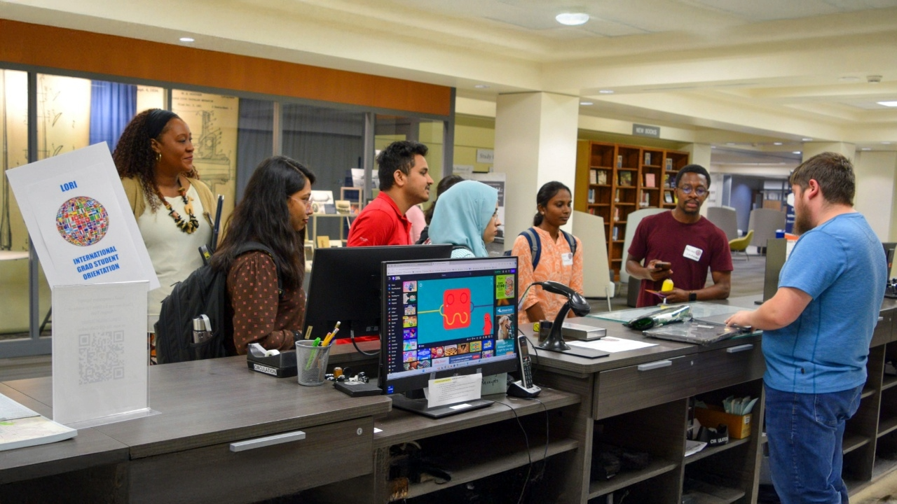Grad students surround the circulation desk in RBD Library, with a sign that says 