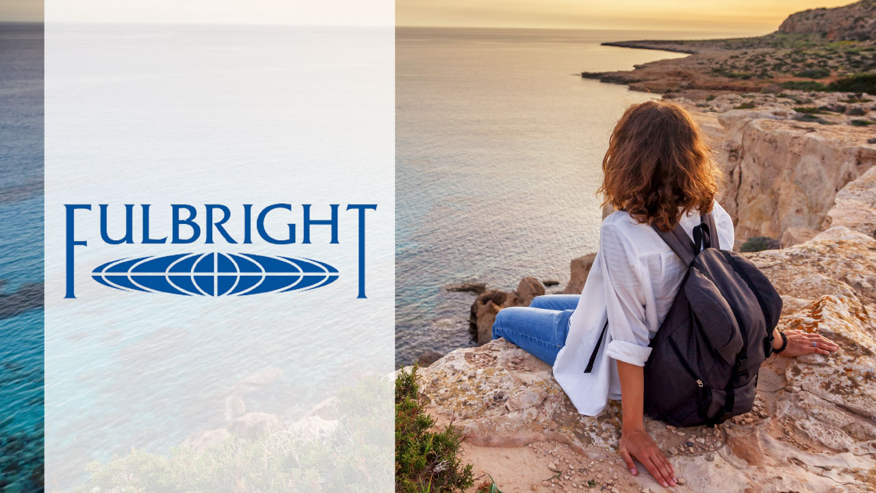 A person with curly hair, wearing a white shirt and blue jeans, sits on a rocky cliff overlooking the ocean at sunset. The person has a black backpack and is gazing towards the horizon. On the left side of the image, there is a vertical white banner with the word 'FULBRIGHT' in blue capital letters and an oval-shaped globe logo beneath it.