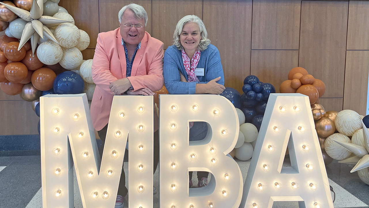 Peter and Sarah Stanwick lean on large MBA display sign