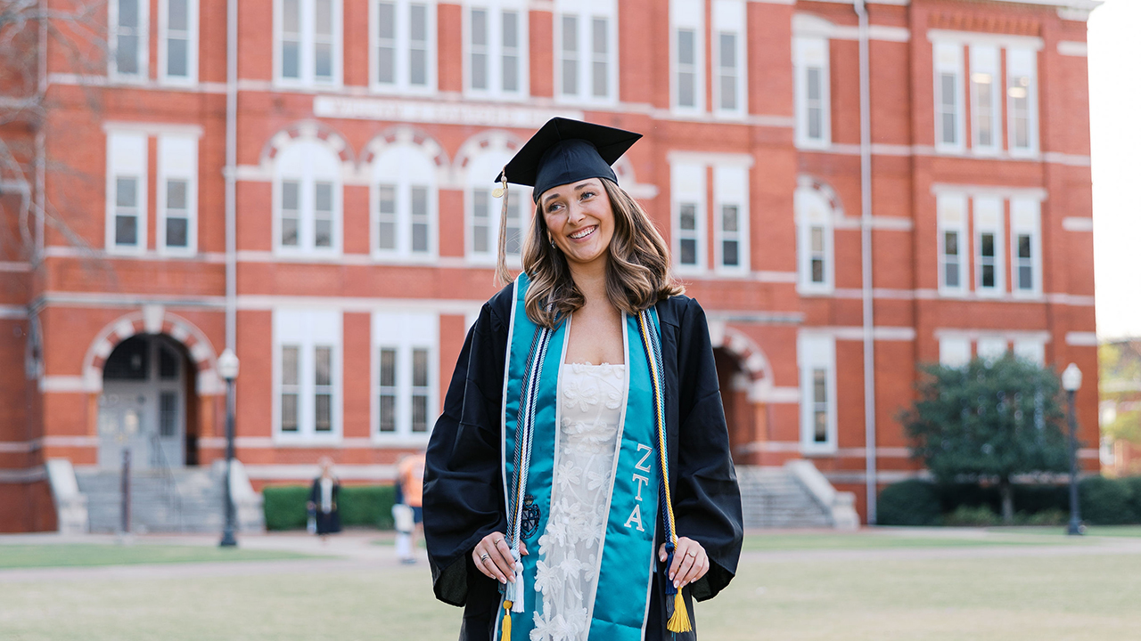 Auburn woman student in cap and gown outdoors