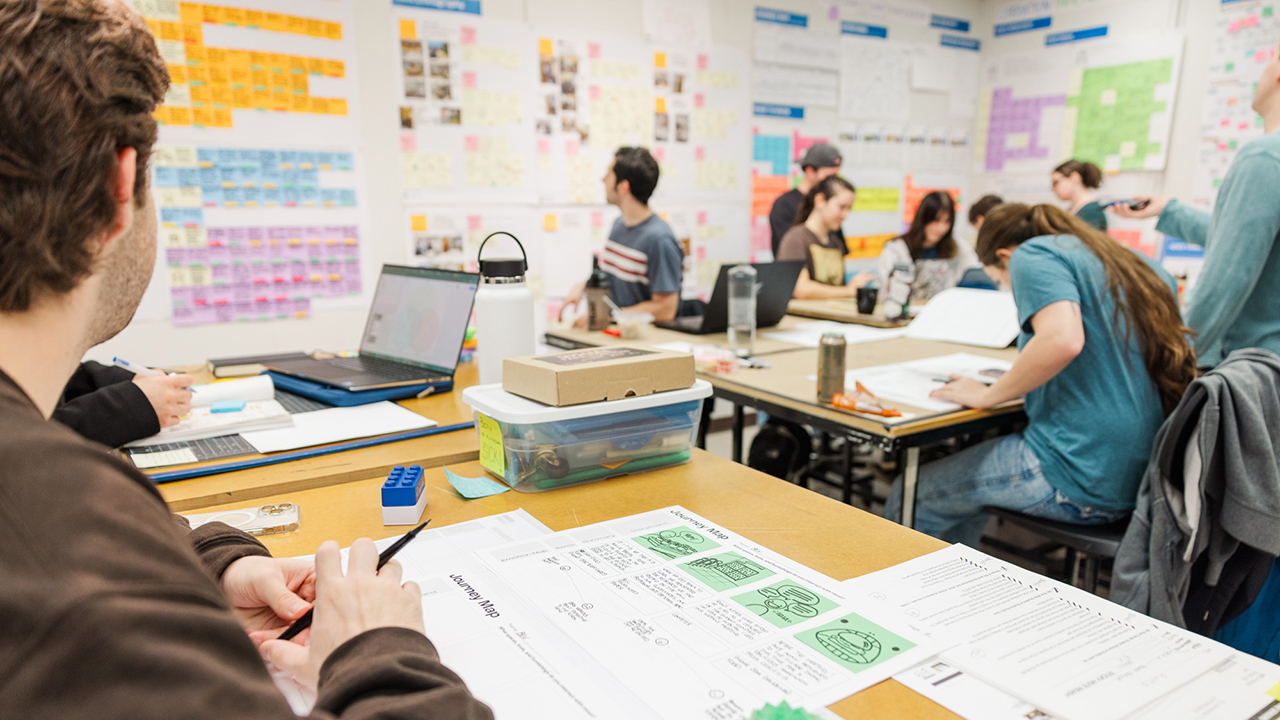 An industrial design student examining notes and feedback on a wall in studio
