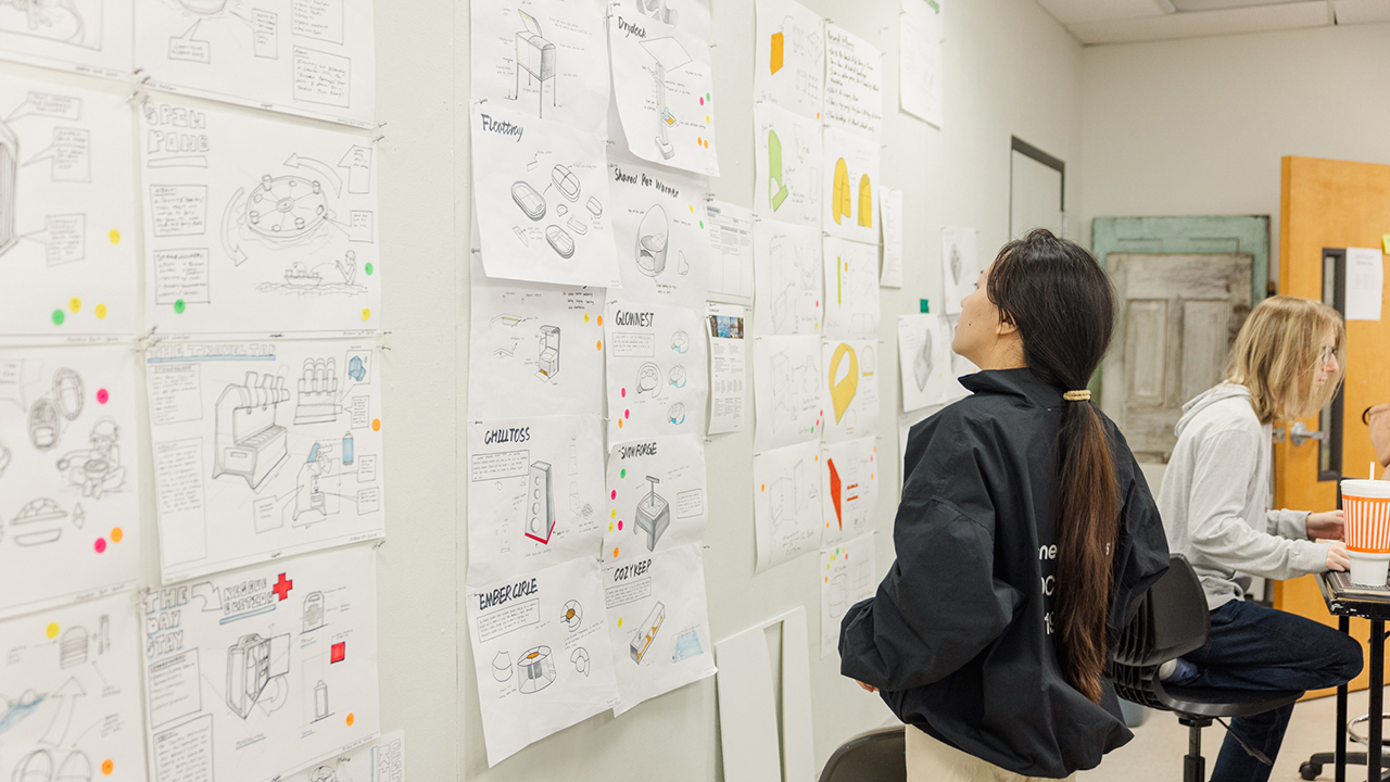Student examining sketches on a wall in an industrial design studio