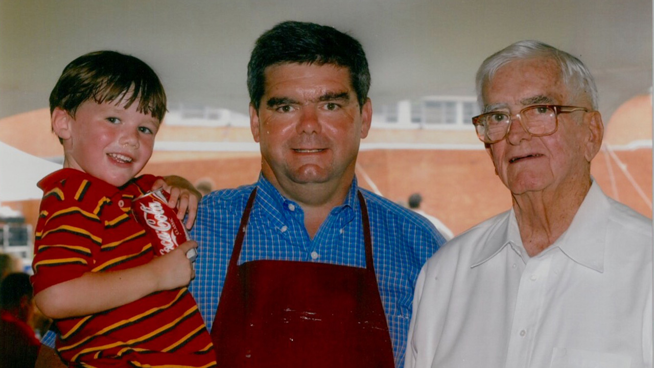 Photo of a man holding a small boy while standing next to his father