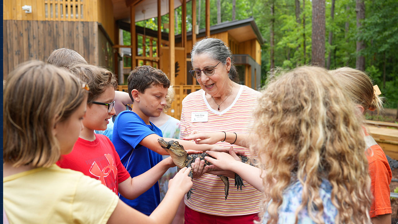 Emily Kling holds a small alligators for students to touch in front of the Environmental Education Building