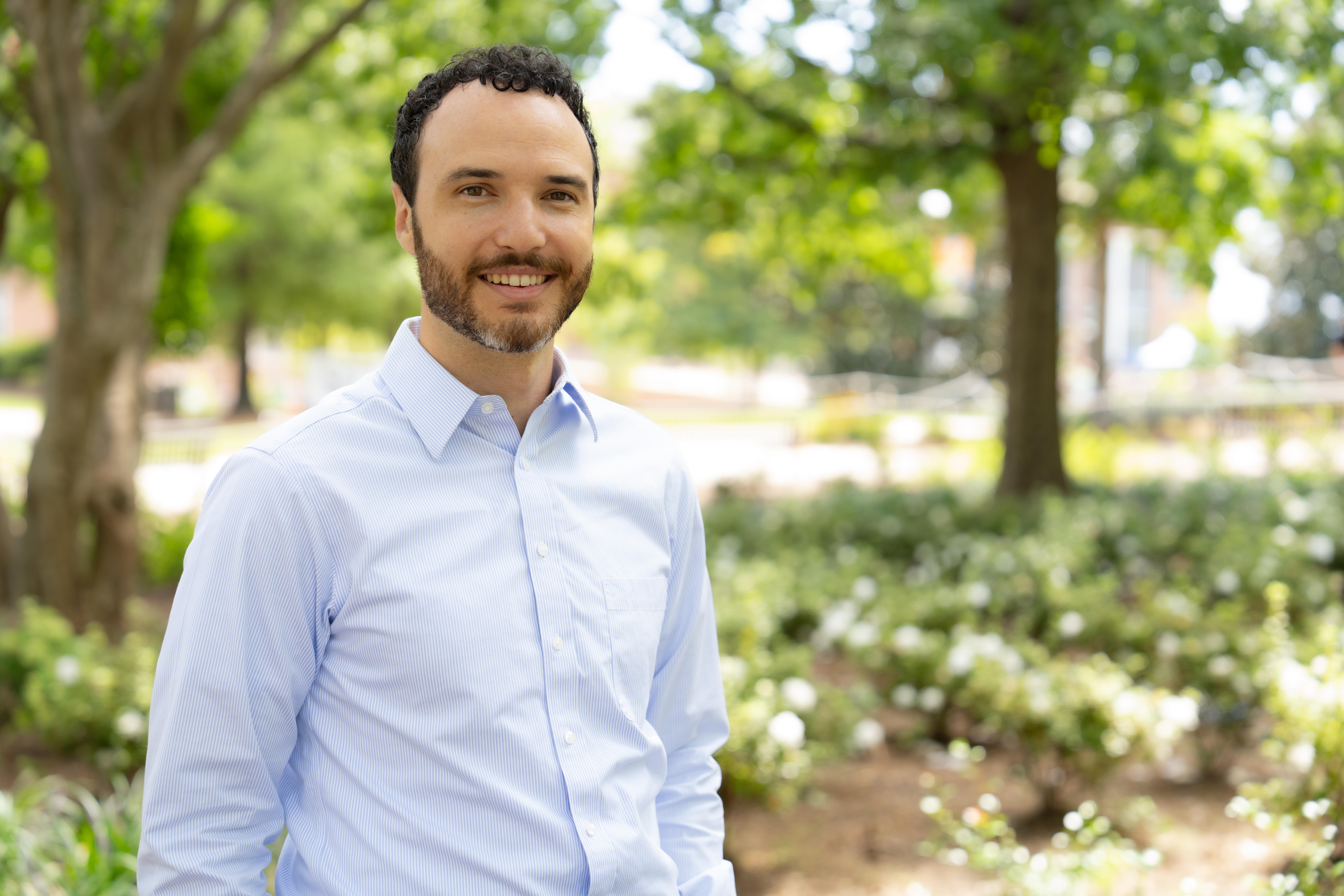 Zach Walsh, assistant professor of mathematics at Auburn University, standing outdoors on campus with trees and flowers in the background