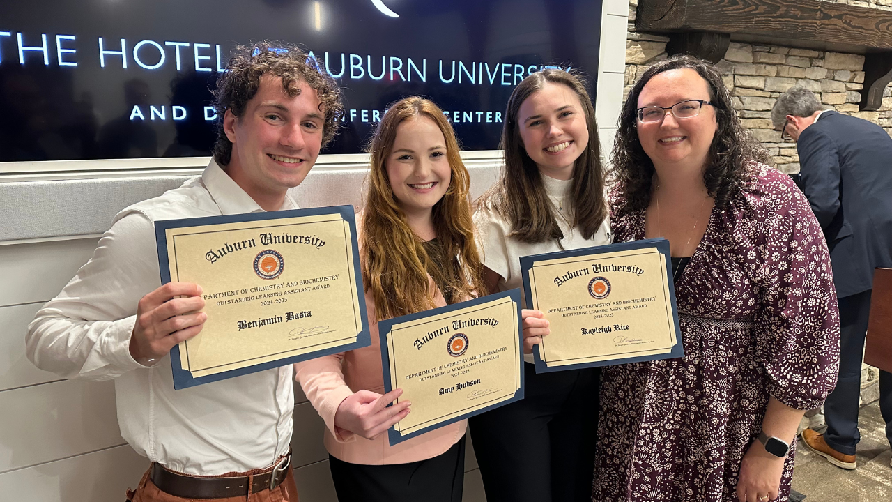 Four individuals stand together indoors, smiling and holding award certificates from Auburn University.