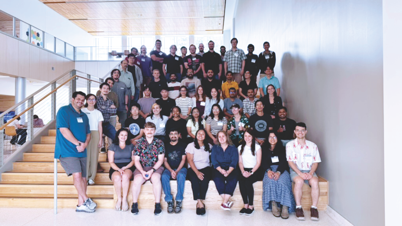 A large group of men and women pose for a photo on a staircase inside a bright, modern building during a biophysics workshop.