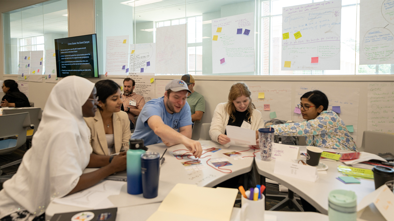 Small group of participants seated at a table, using papers and string for a collaborative teaching activity at AUSSI.