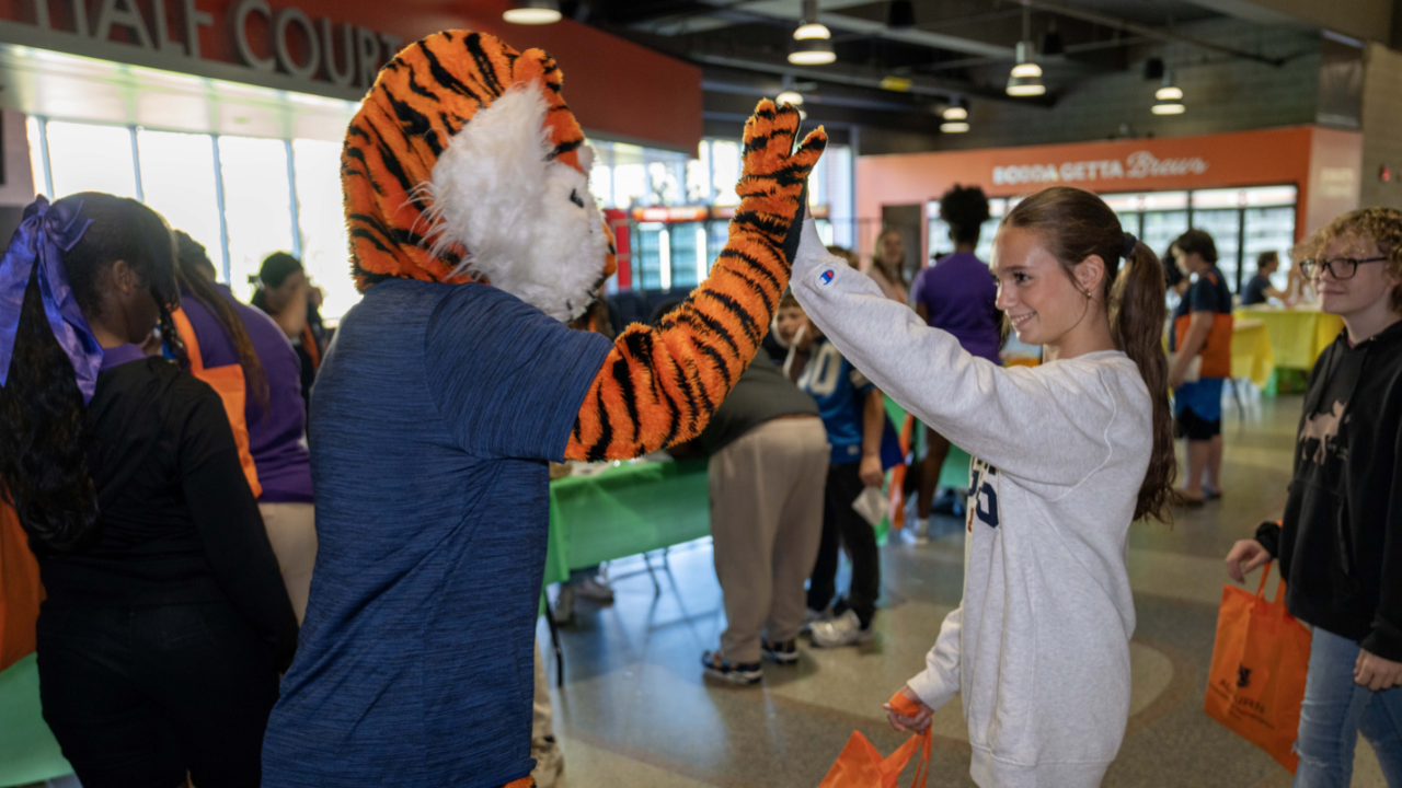 Auburn’s tiger mascot high-fives a student carrying an orange tote bag during the Destination STEM Expo.