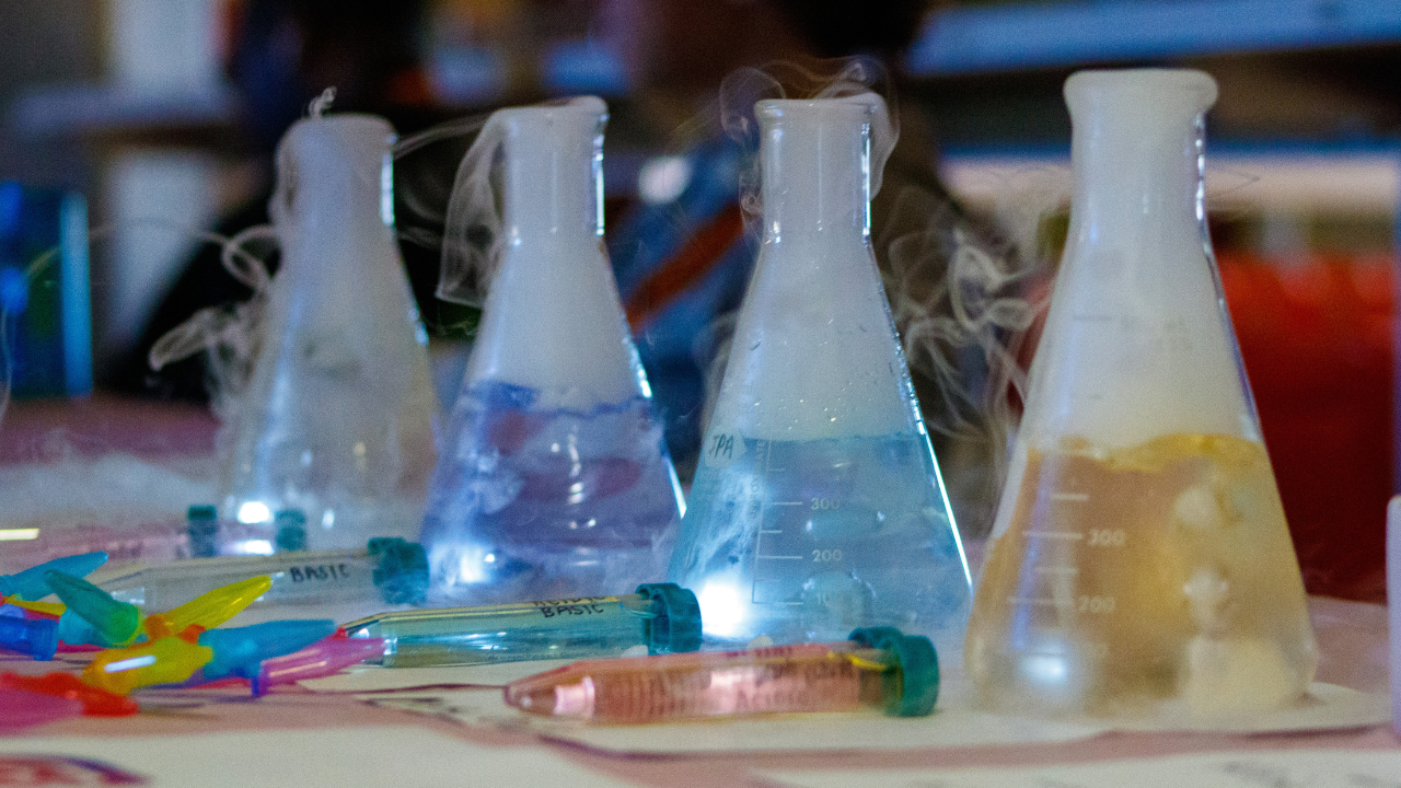 Beakers filled with colorful liquids emit vapor during a chemistry demonstration.