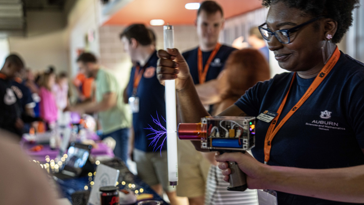 A volunteer demonstrates how plasma travels through a glass tube using an electric discharge device during a STEM exhibit.