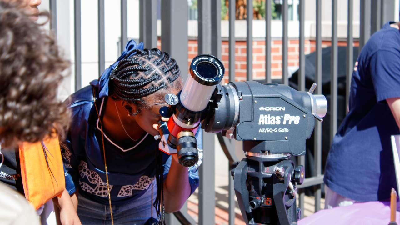 A student looks through a telescope at an outdoor astronomy station.