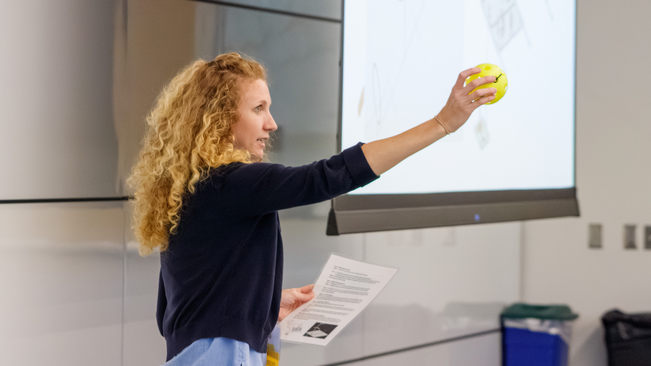 A presenter holds up a yellow ball while explaining a classroom robotics activity during a SERC session.