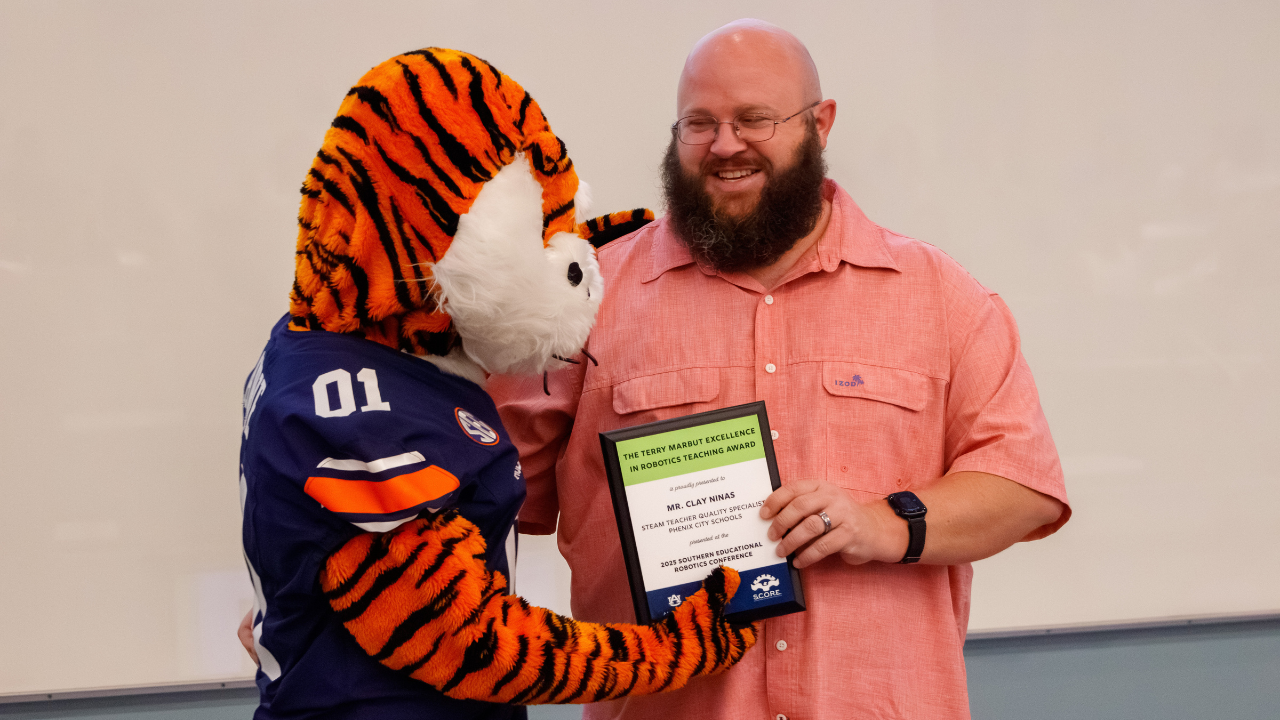 Aubie presents the Terry Marbut Excellence in Robotics Teaching Award to Clay Ninas at the 2025 SERC conference.