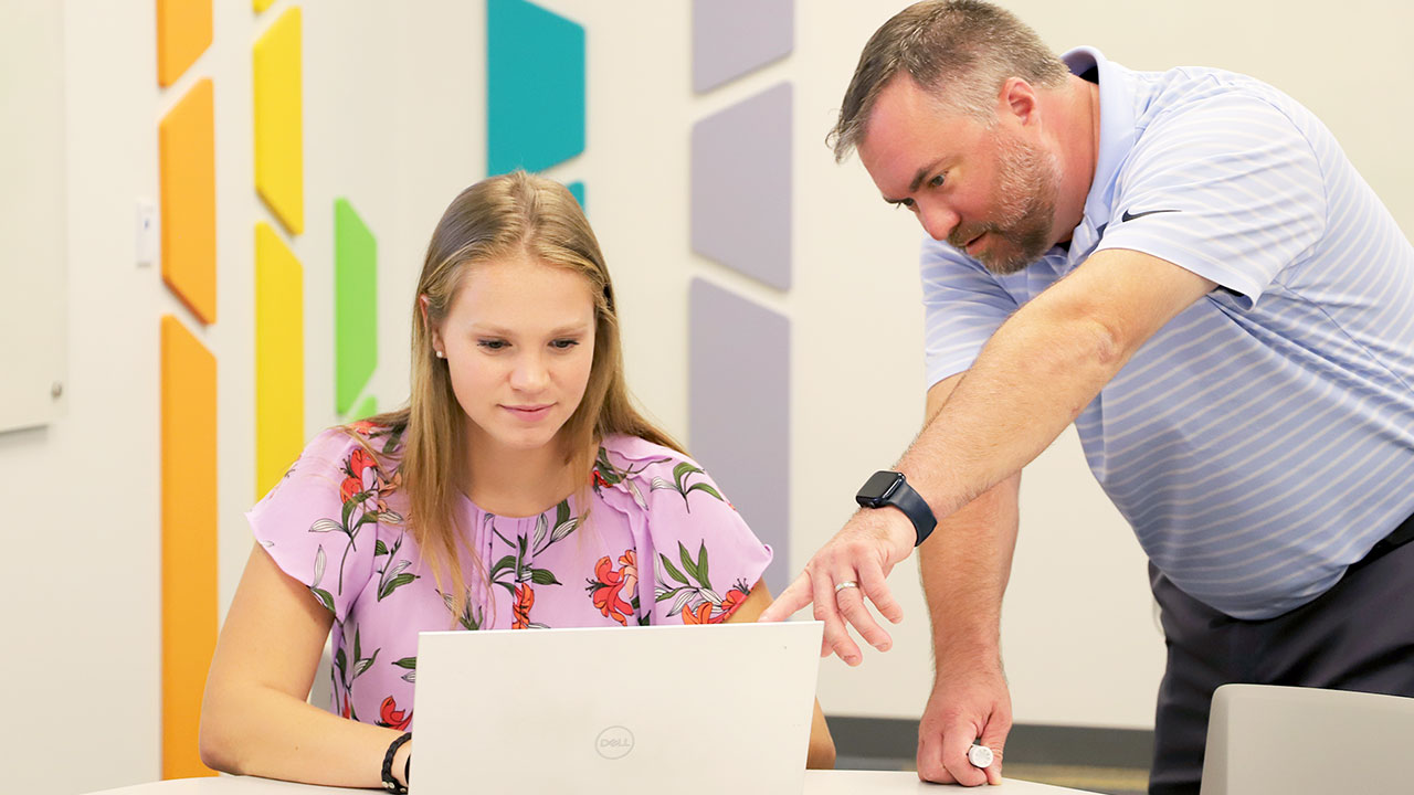 A student is pictured with a professor looking at a laptop screen.