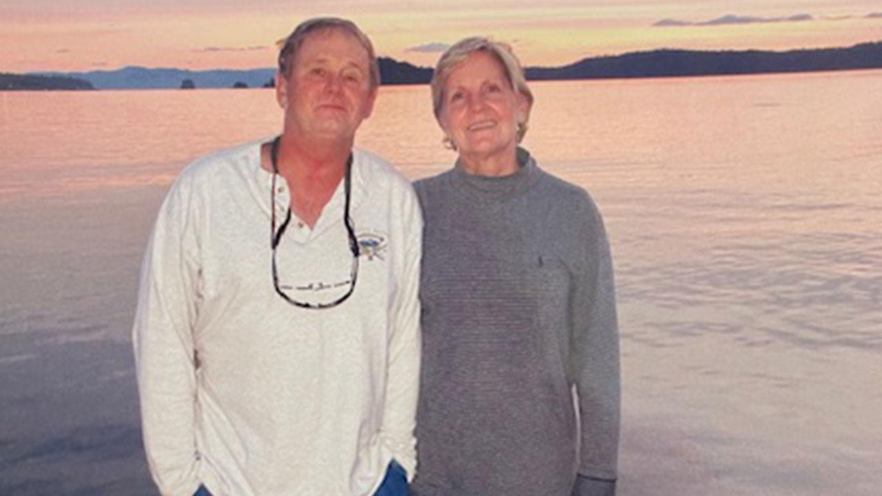 Mike and Joan Newman are pictured outdoors with a body of water behind them.