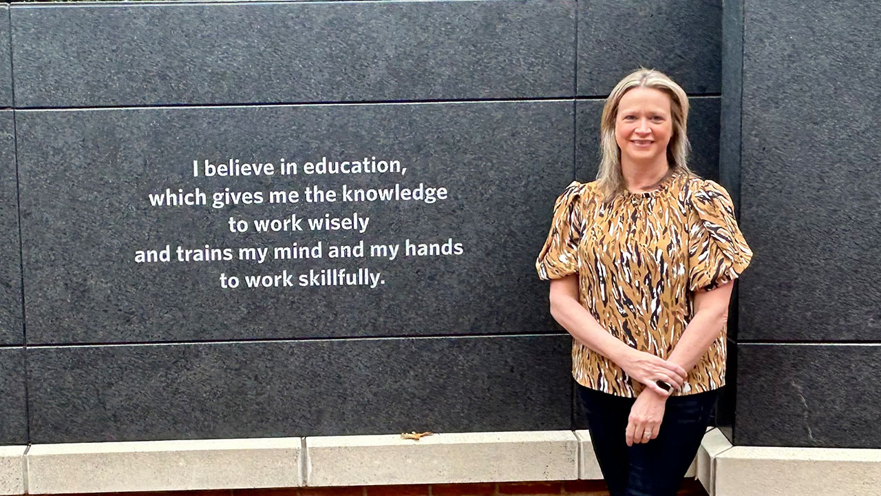 Molly McNulty is pictured outdoors next to a wall with an engraving of the Auburn Creed