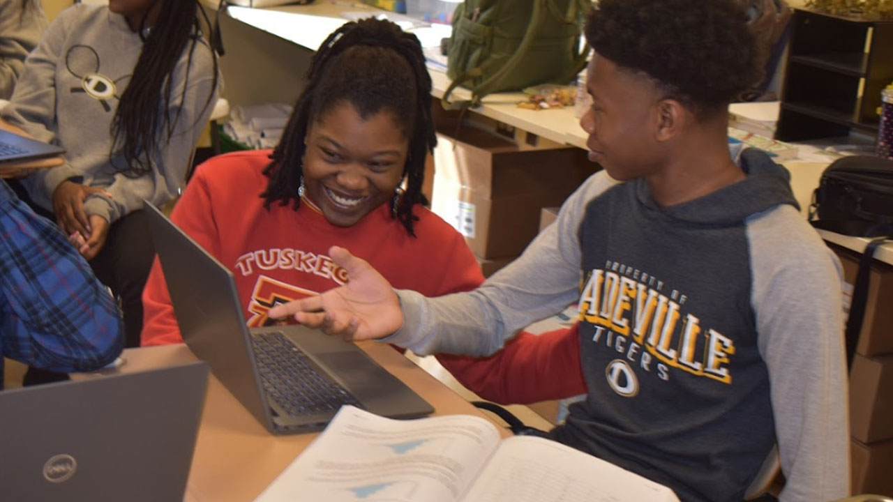 A student teacher is pictured working with a student as he points to a computer screen.