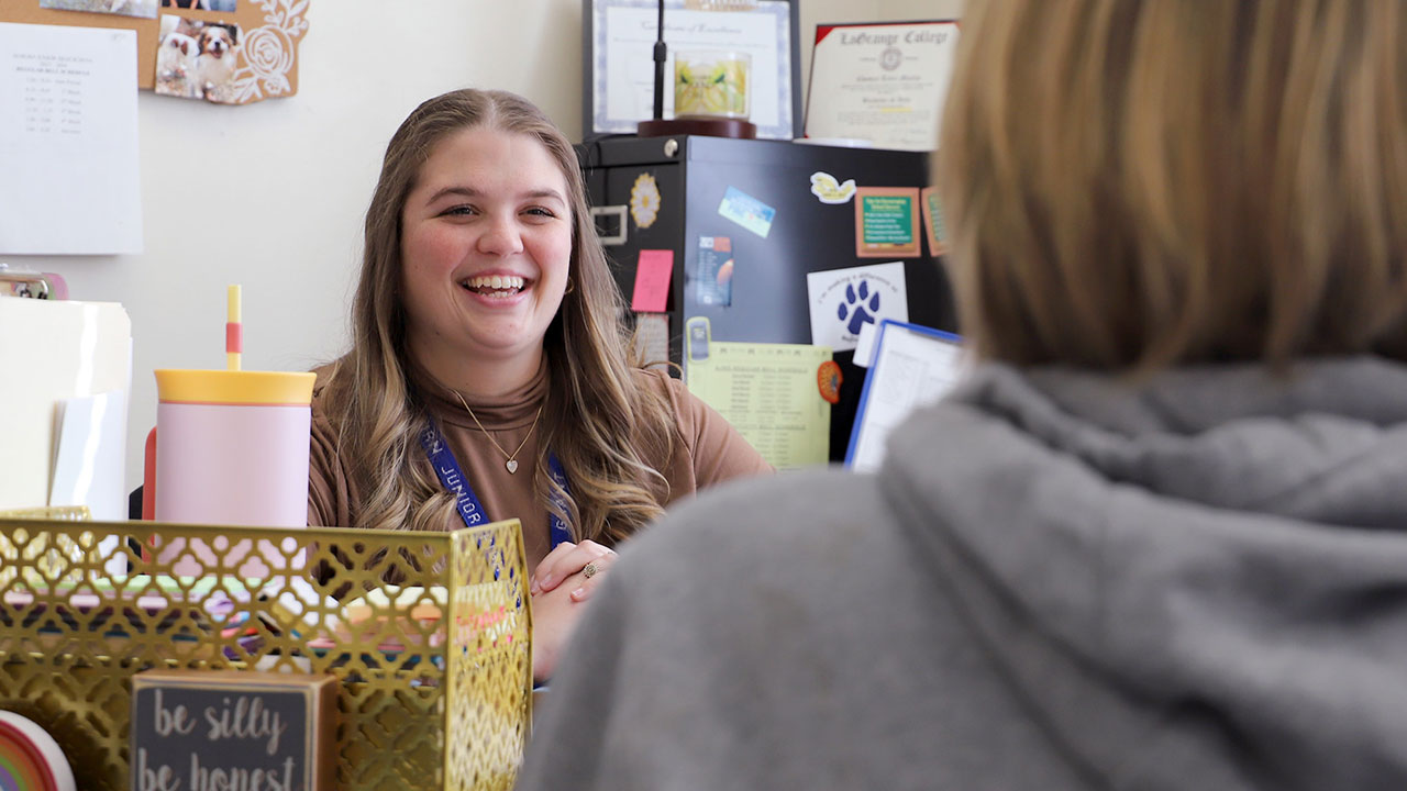 School counselor Tyler Grant is pictured at a desk and talking to a student inside her office.