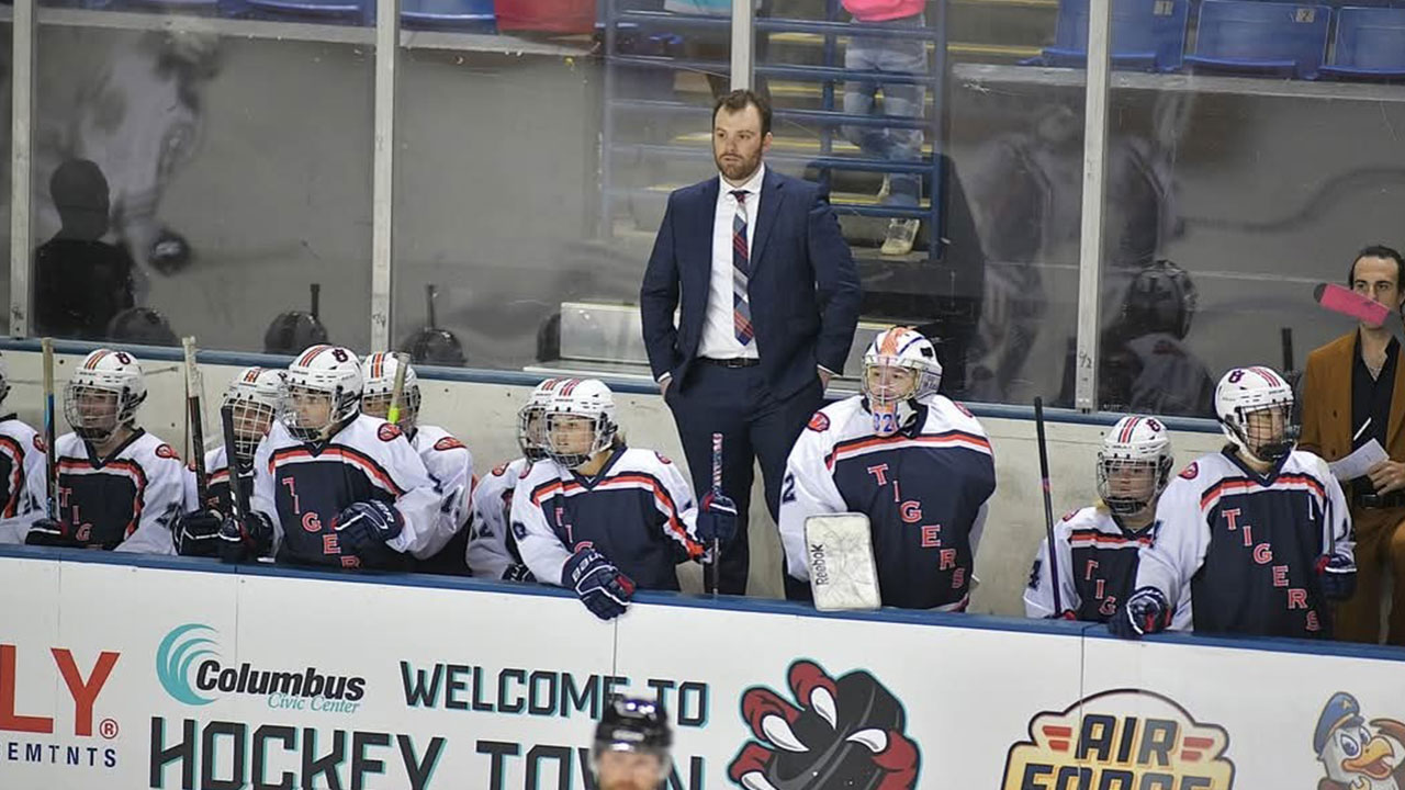 Jack Rosenhammer is pictured standing behind the women's ice hockey team that he coaches.