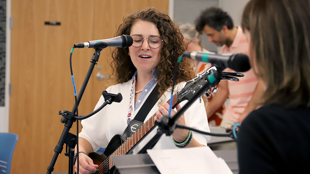 A group photo of those in the College of Education faculty band is depicted inside a music education lab.