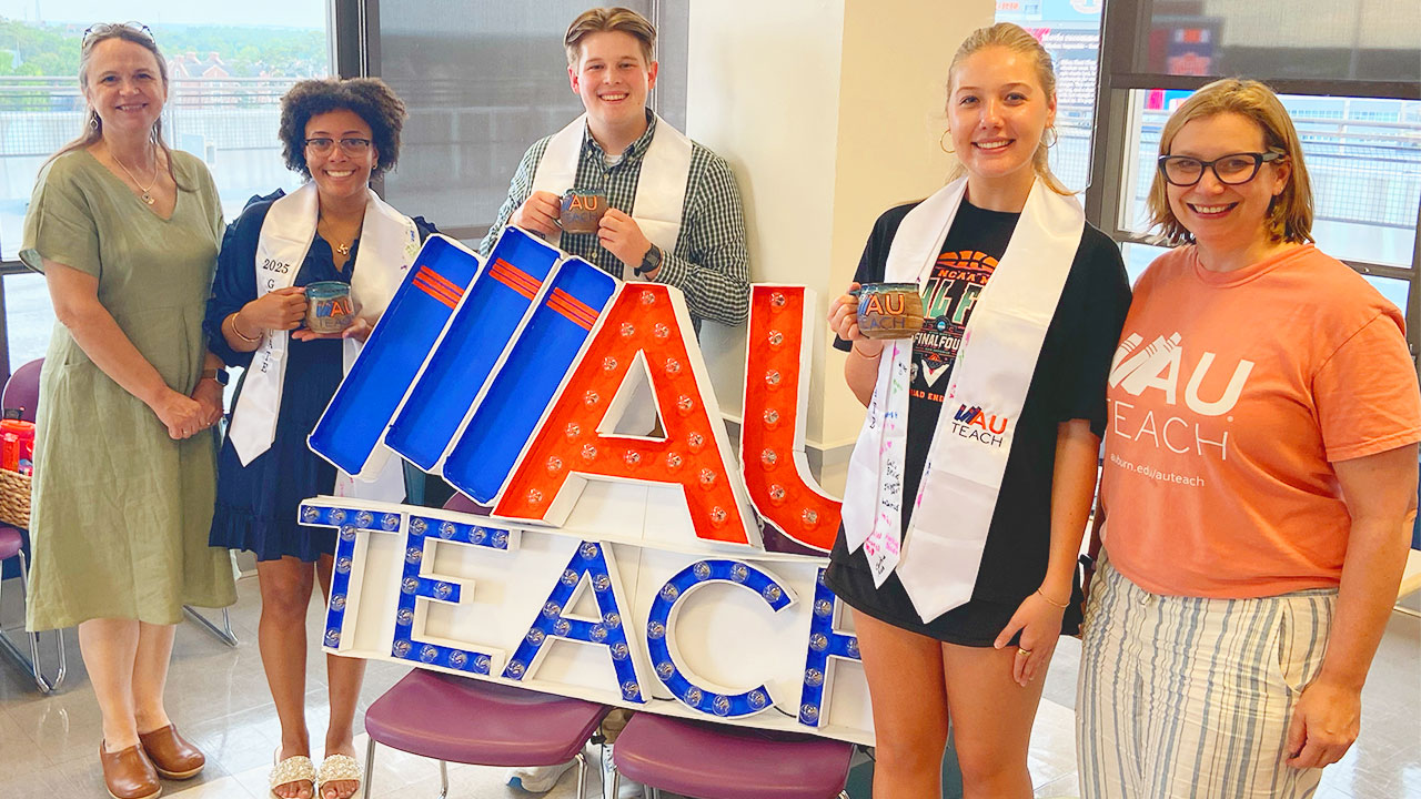 A group of students is pictured with faculty and staff around a sign that states AU Teach