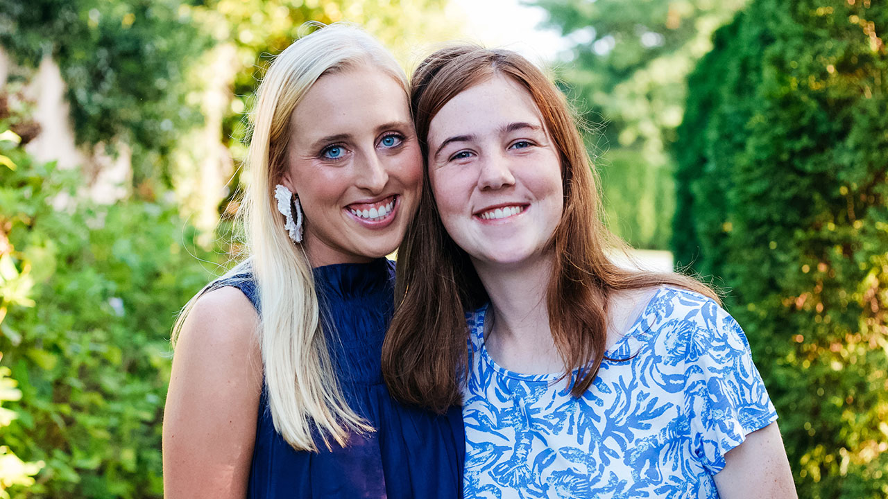 Two women are pictured side by side smiling outdoors,