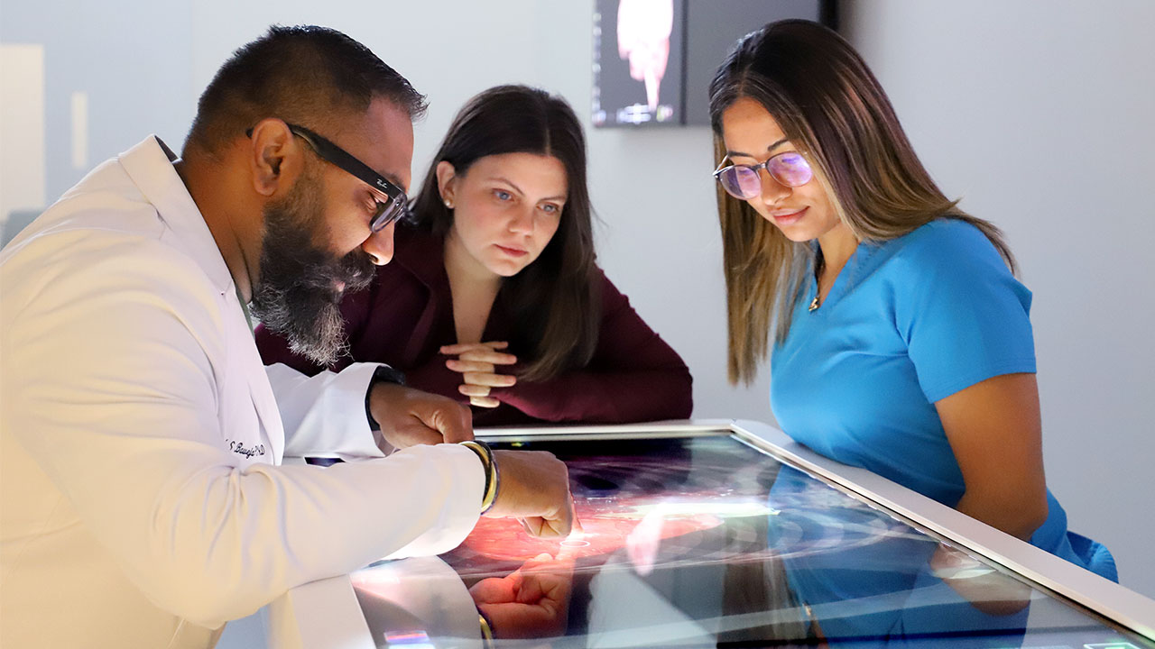 A professor and students stand around a simulation table in a lab.