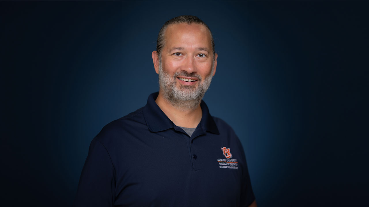 Brian Phillips smiles in a posed photo with a dark background behind him.