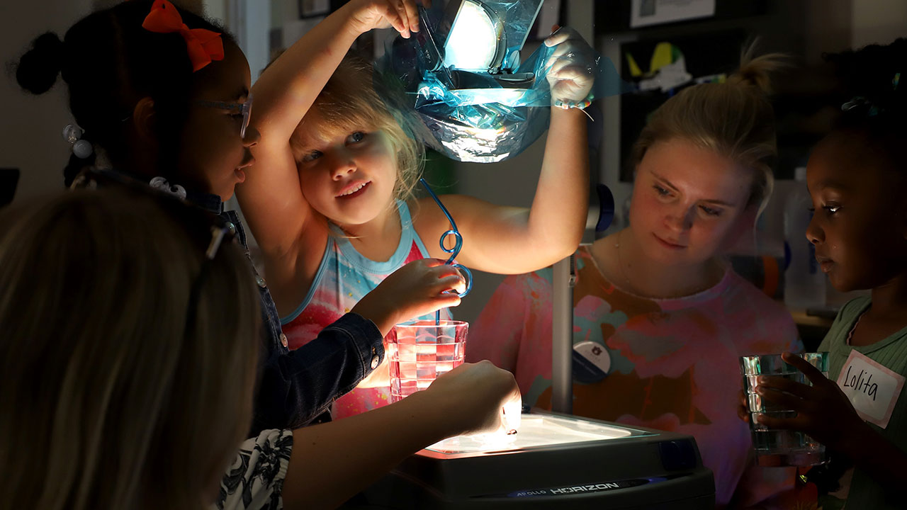 Students and children participate in an exercise involving brilliant lights inside a classroom.