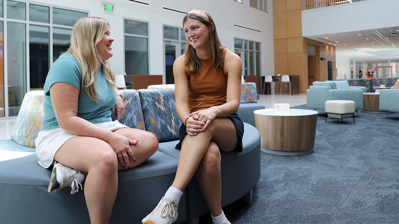 Students Zadie Lakin (left) and Anna Poole talk with one another while sitting on a couch in the new College of Education building.