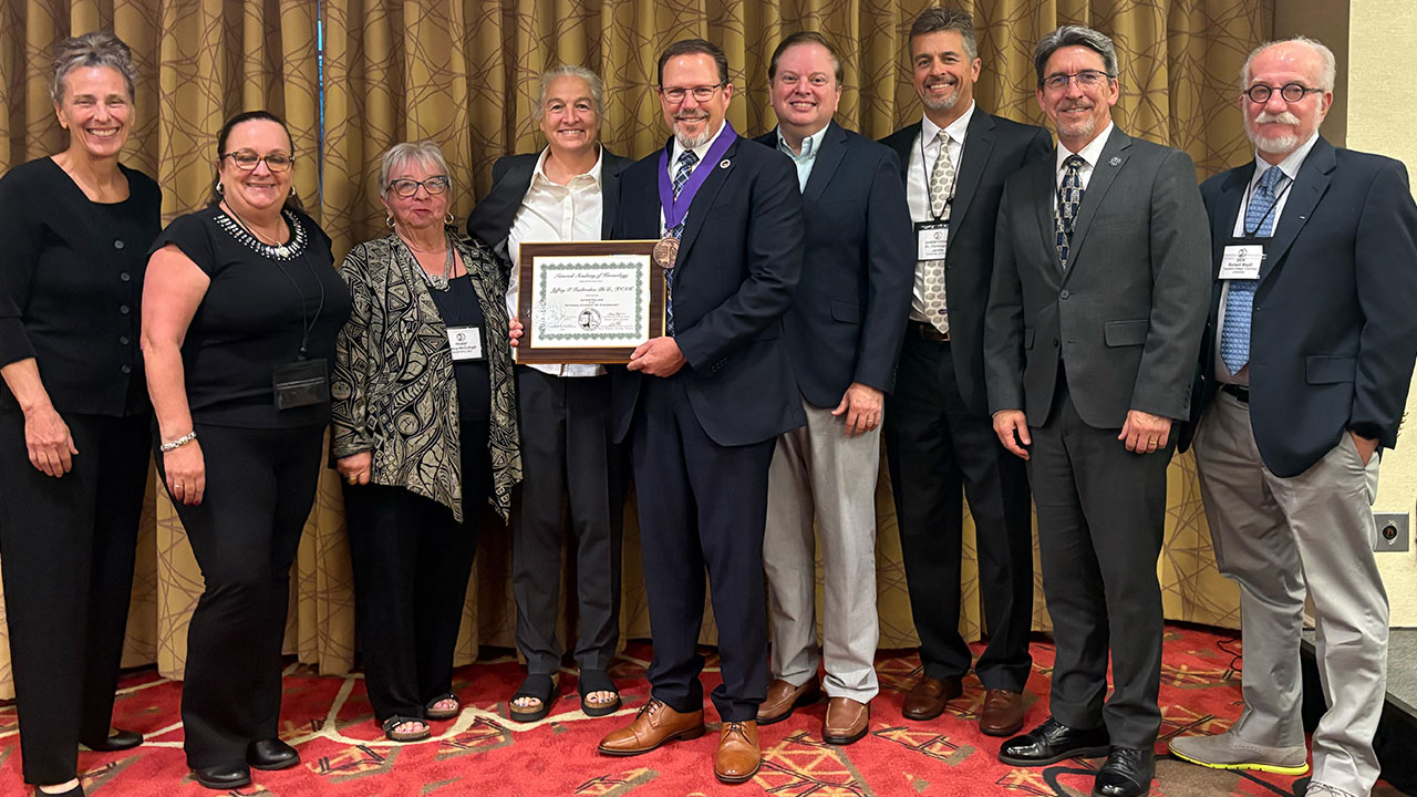 Jeffrey T. Fairbrother, dean of Auburn University’s College of Education is pictured holding a certificate and posing for a photo indoors with several other NAK Fellows. 