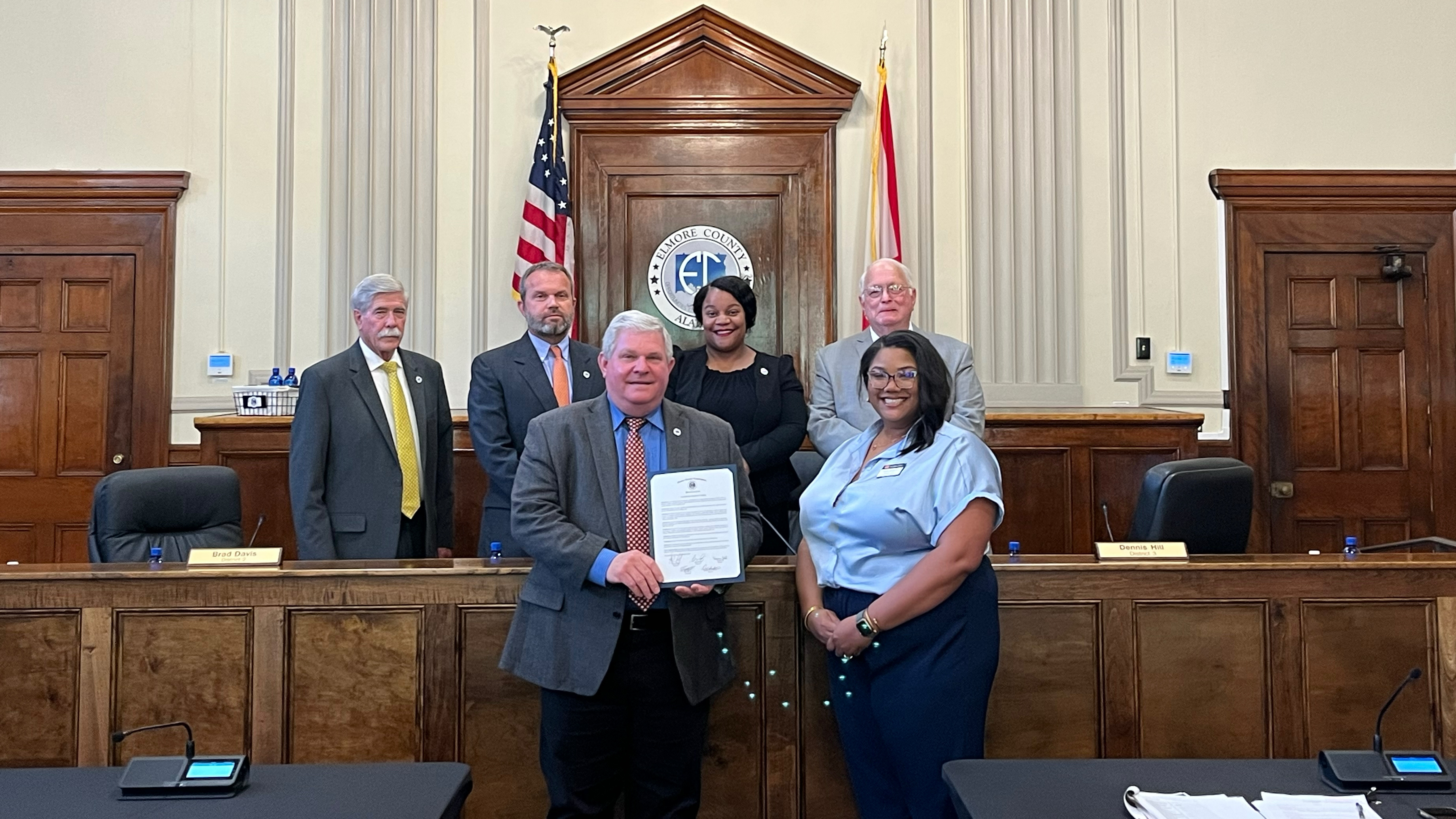Six members of the Elmore County Commission flank Imma Sanders, GEAR UP Achieve Region 9 School Liaison, as she accepts their proclamation of National GEAR UP Week in Elmore County.