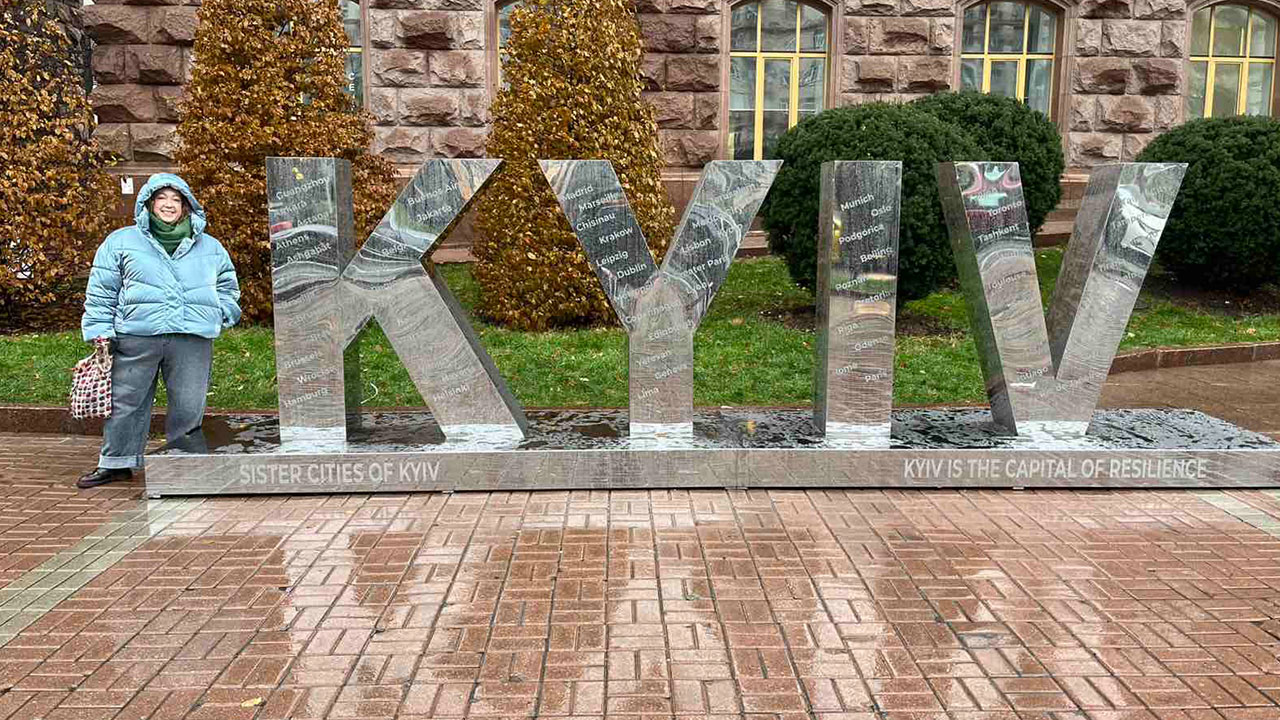 Amanda Denney is pictured standing outdoors next to large letters that spell out KYIV, the capital of Ukraine.