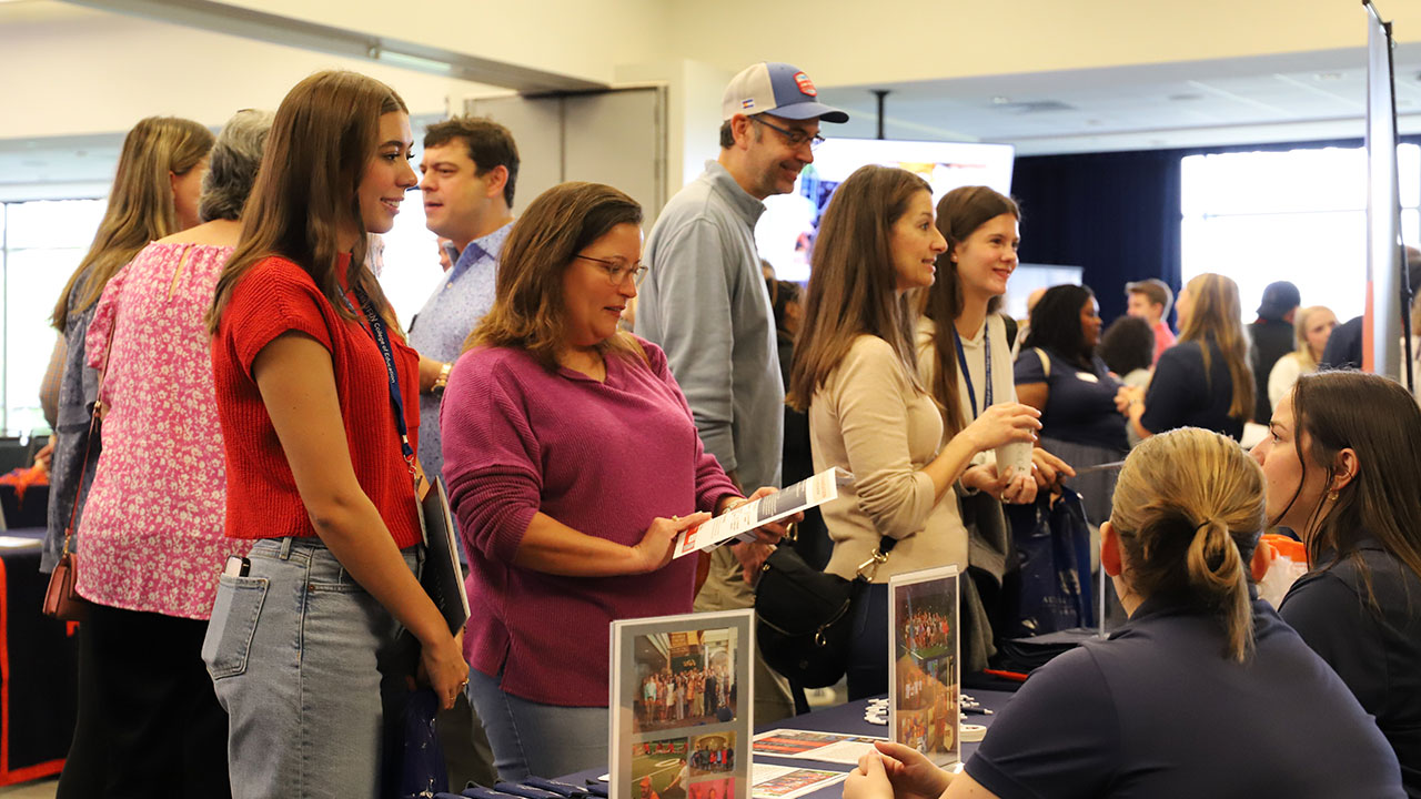 Several students and their parents talk to workers seated at tables at a past Fall Preview Day event.