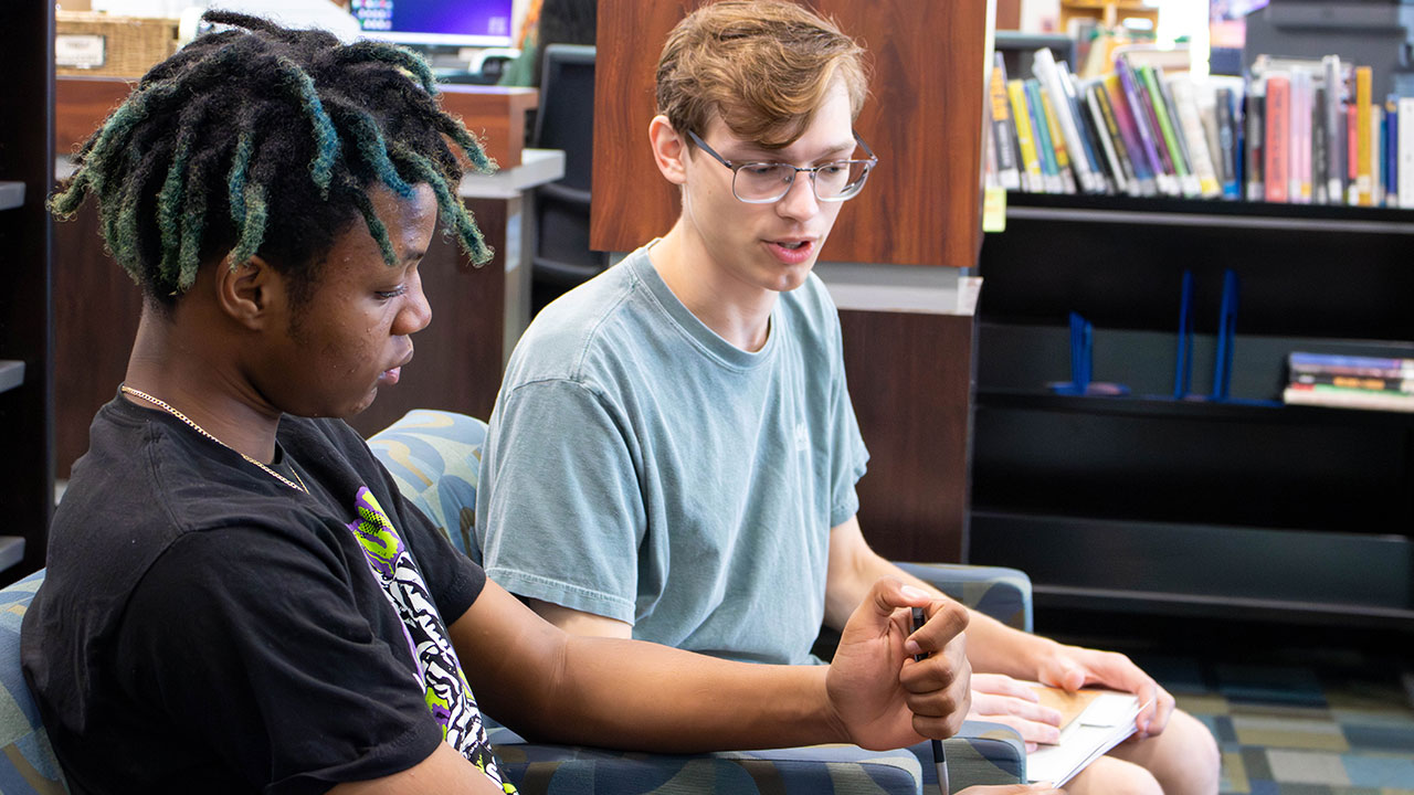 A preservice teacher works with a ninth grader, discussing a book together