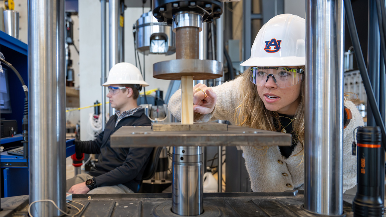A woman looks at a piece of wood in the advanced structural engineering lab. 