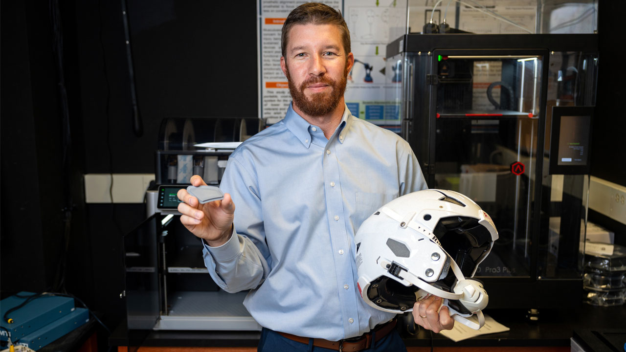 Michael Zabala holds a helmet and the ear hole covers created by his business, XO Armor