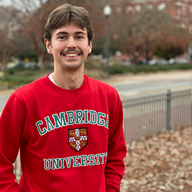 Cameron in Cambridge sweatshirt standing in front of Samford Hall