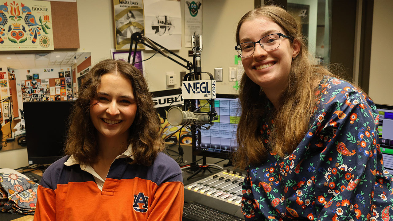 Two girls sitting in the WEGL radio booth with radio equipment and microphones surrounding them.