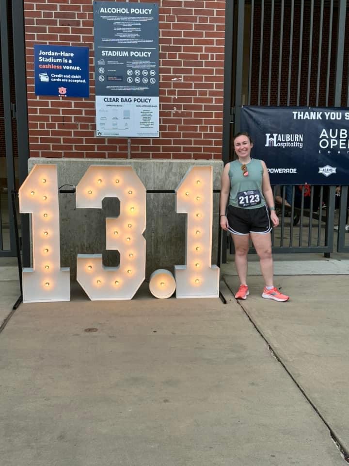 emily after a marathon standing next to a light up sign outside of the auburn stadium