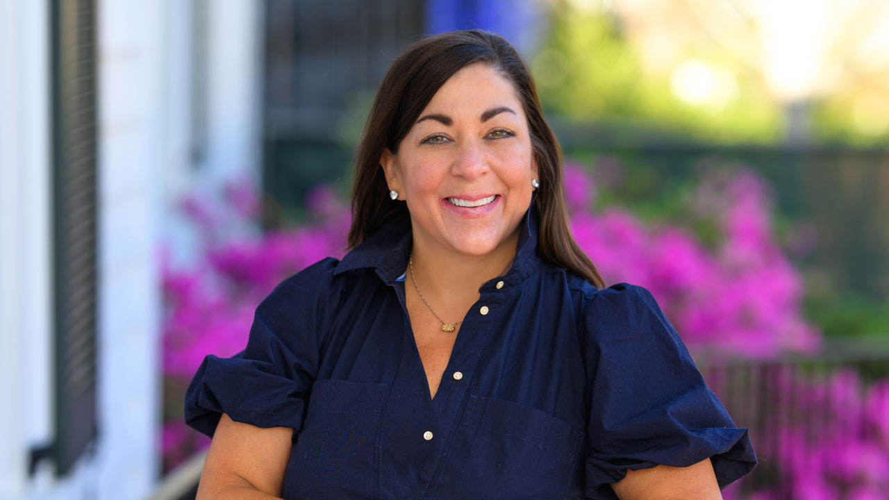 Headshot of Ashley Daniels on the front porch of cater hall with pink azeleas in bloom behind her.